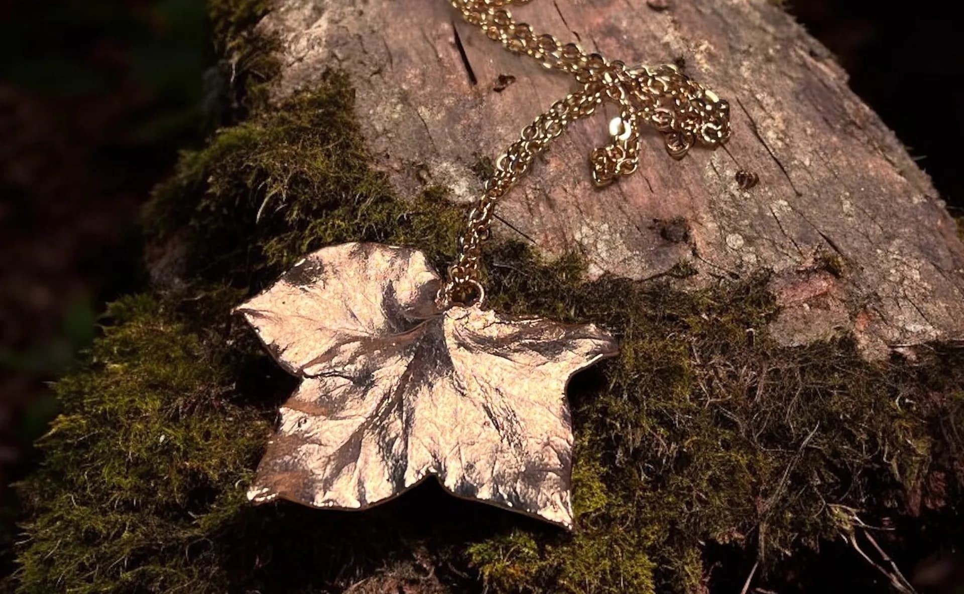 Electroformed copper ivy leaf pendant on a gold chain, resting on a mossy log