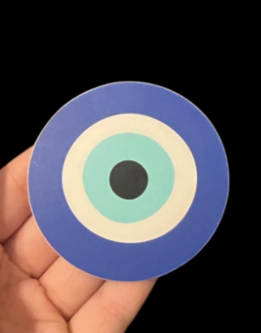Hand holding a round blue, cream and teal evil eye sticker