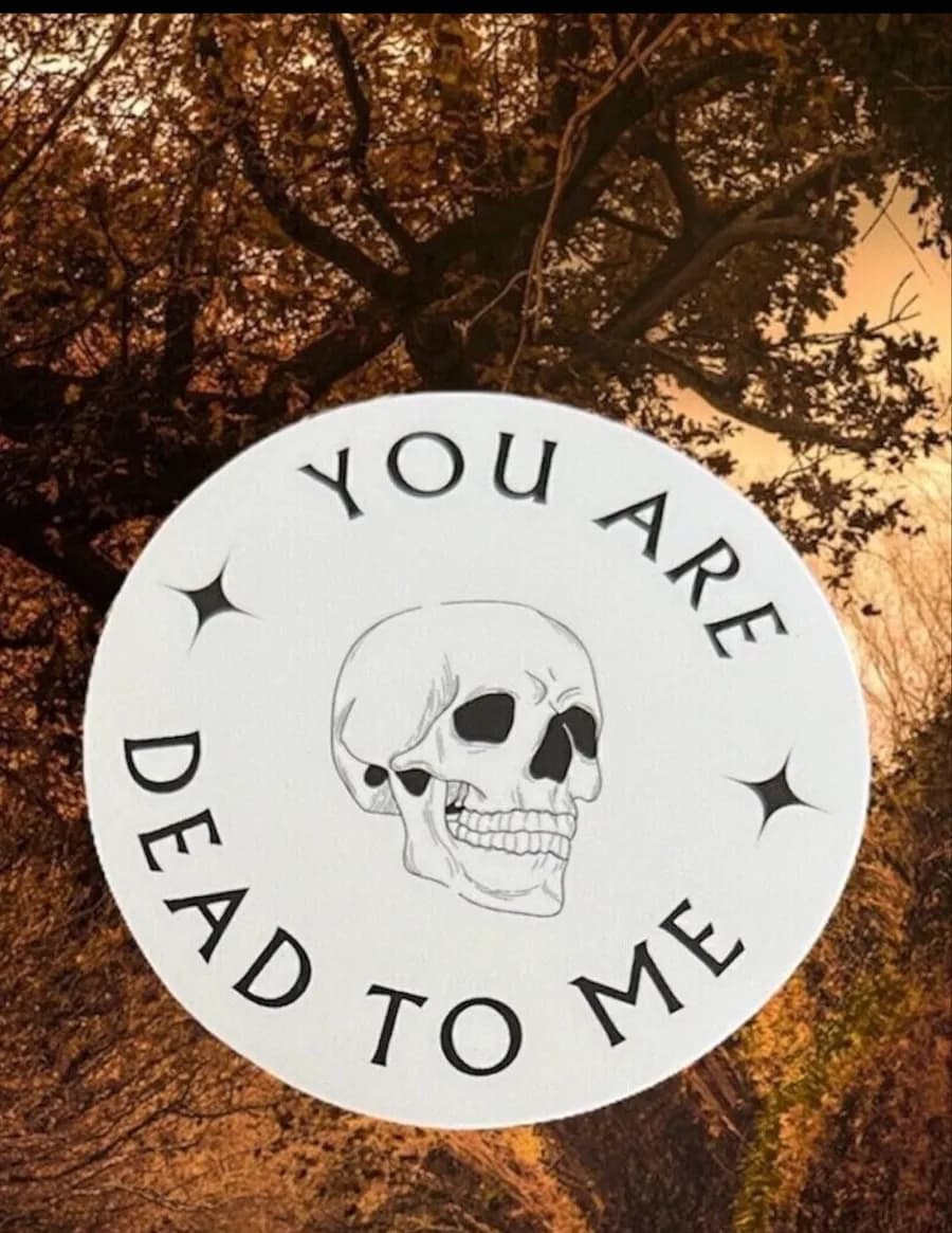 Round white sticker with a skull reading 'You are dead to me' against autumn trees