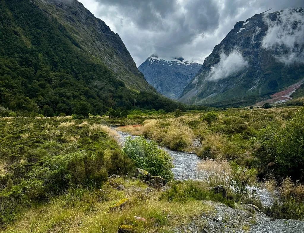 A river winding through a green mountain valley under snow-capped peaks